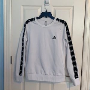 A white sweater with black adidas logos on sleeves